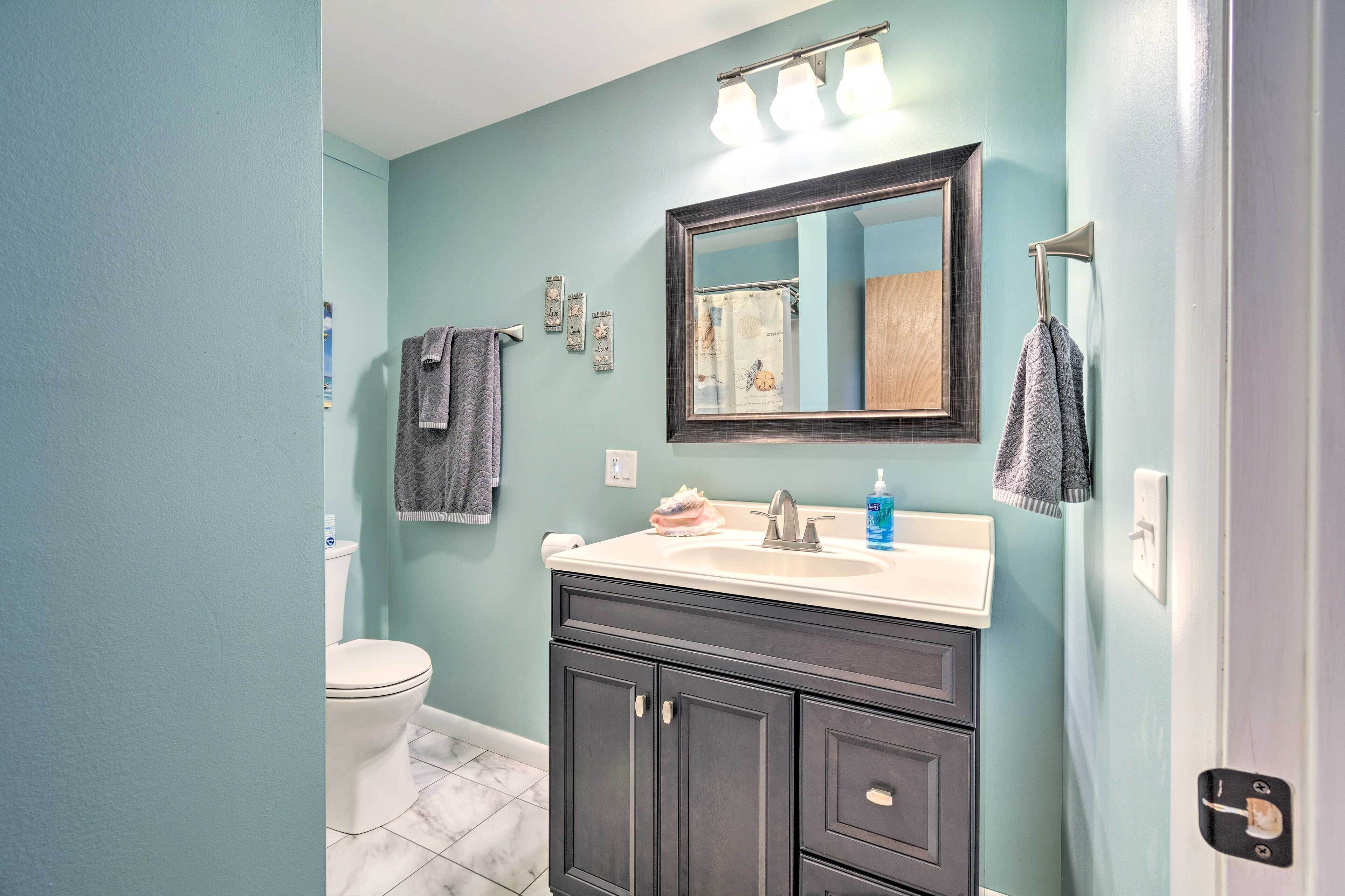 A bathroom with a white toilet, dark cabinets, a mirror with lights, and a towel rack.