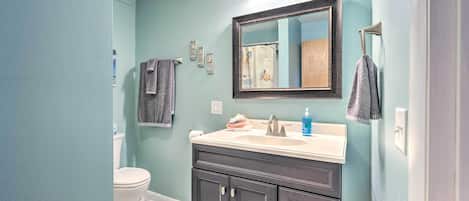 A bathroom with a white toilet, dark cabinets, a mirror with lights, and a towel rack.