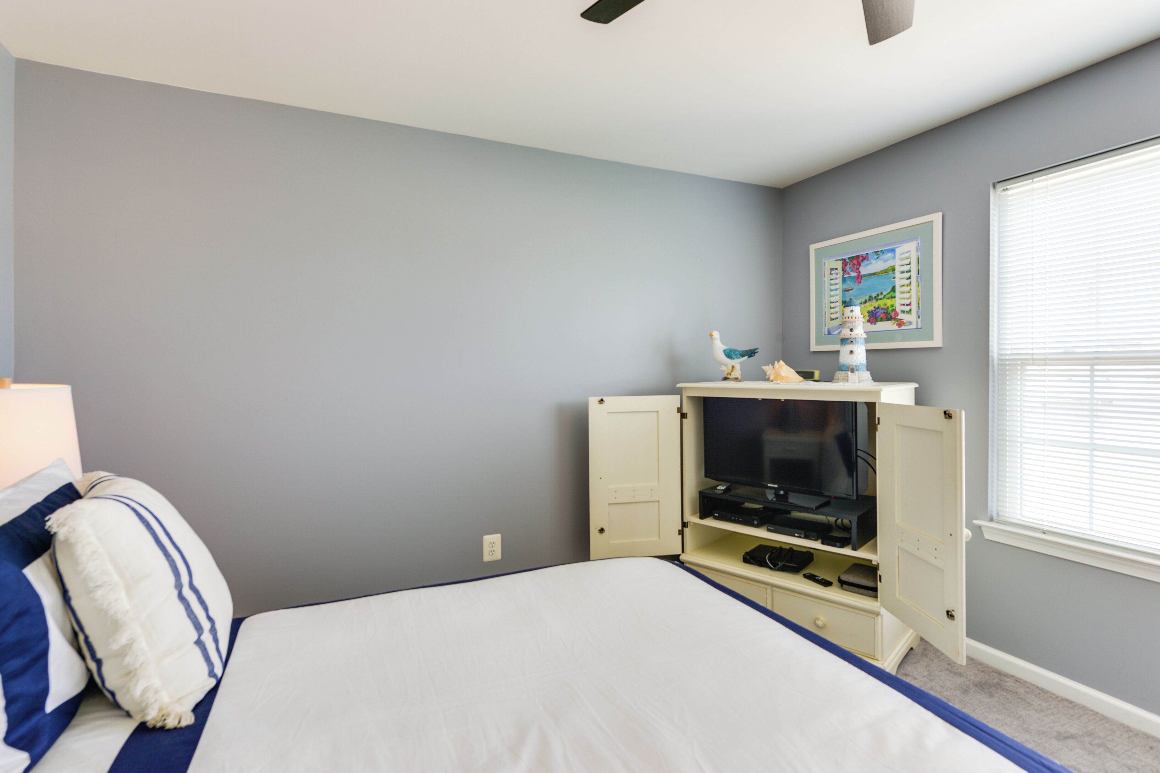 A bedroom with a bed, a TV cabinet, and a window with blinds.