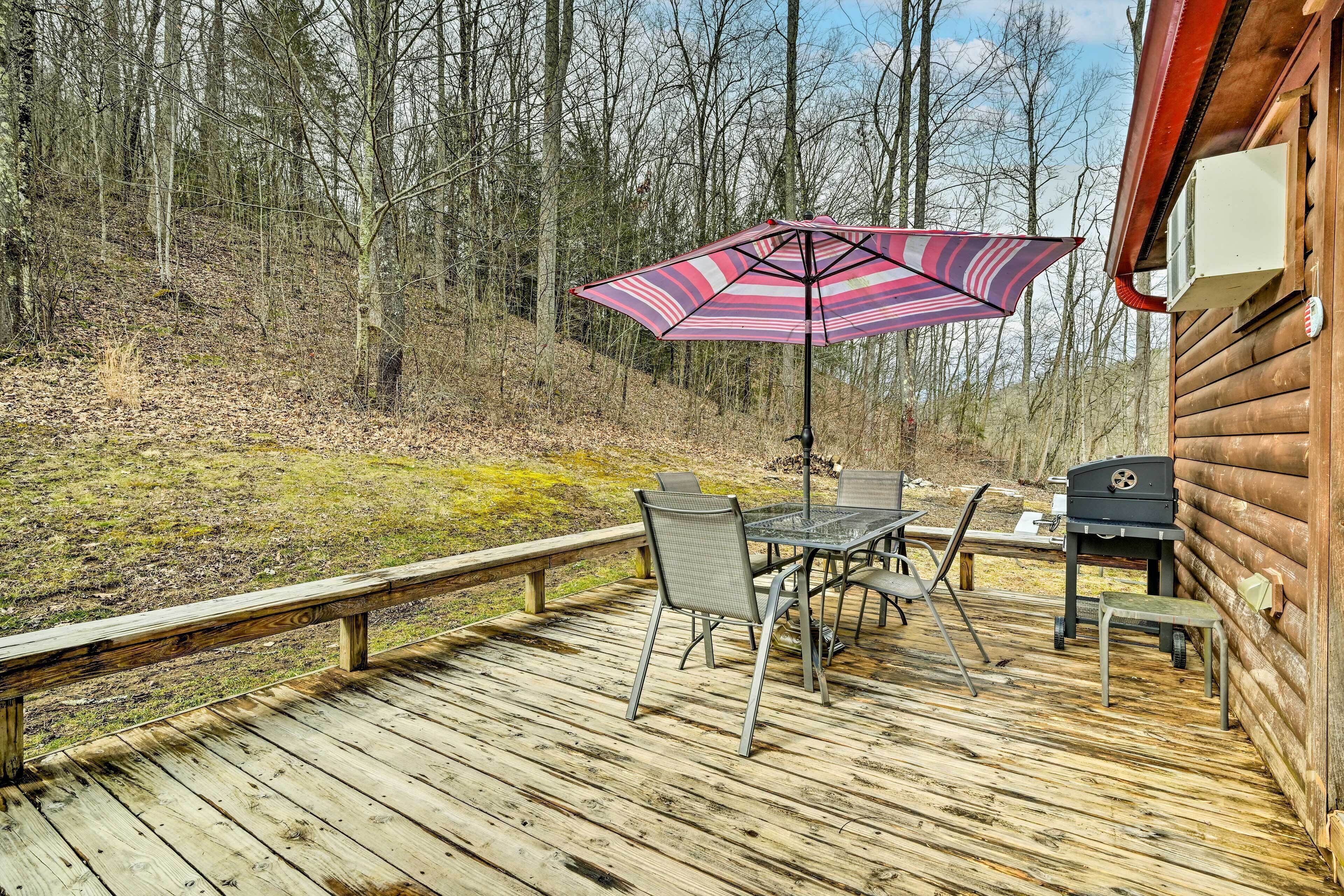 A wooden deck with a table and chairs, a grill, and an umbrella.