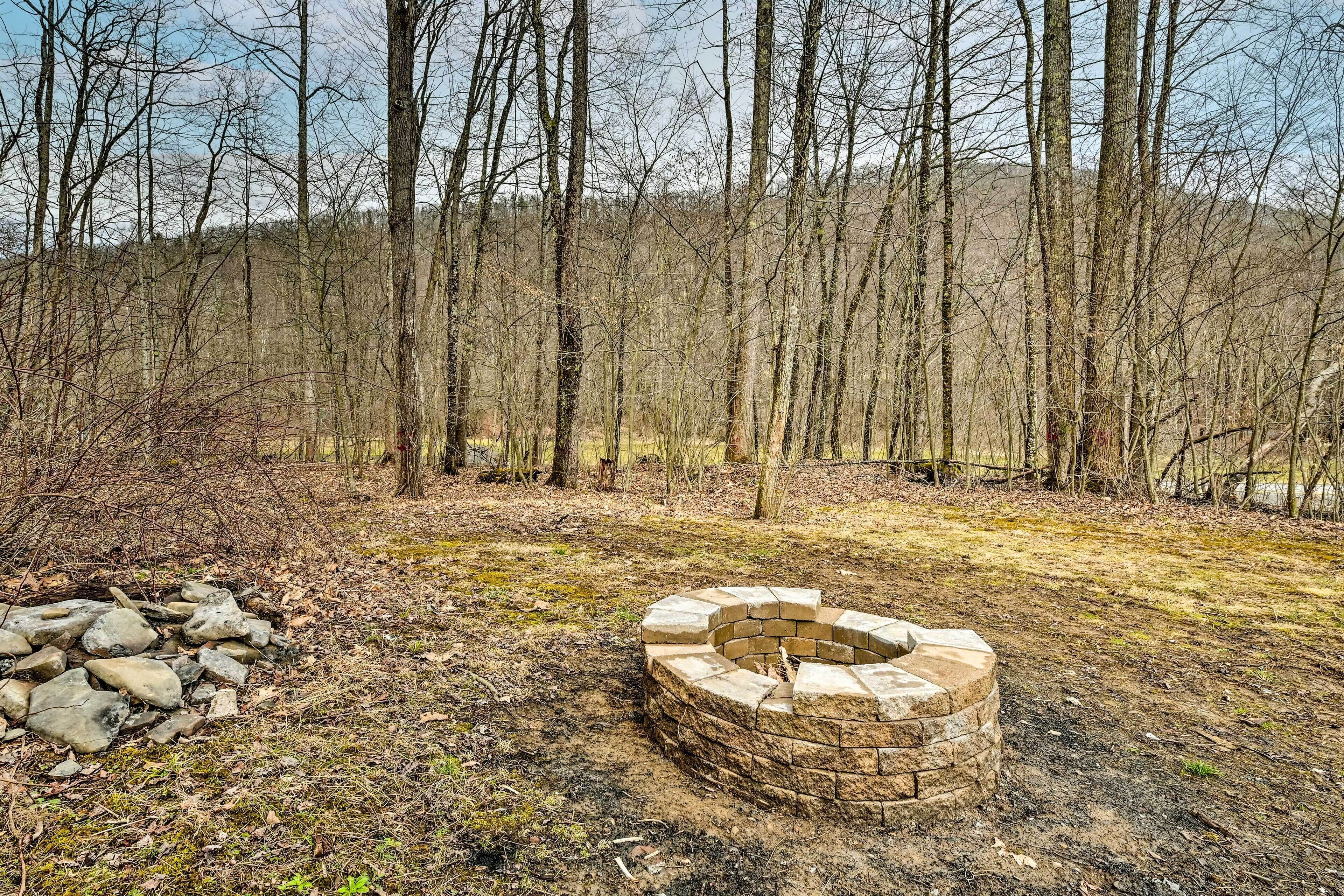 A stone fire pit in a forested area with bare trees and a pile of rocks nearby.