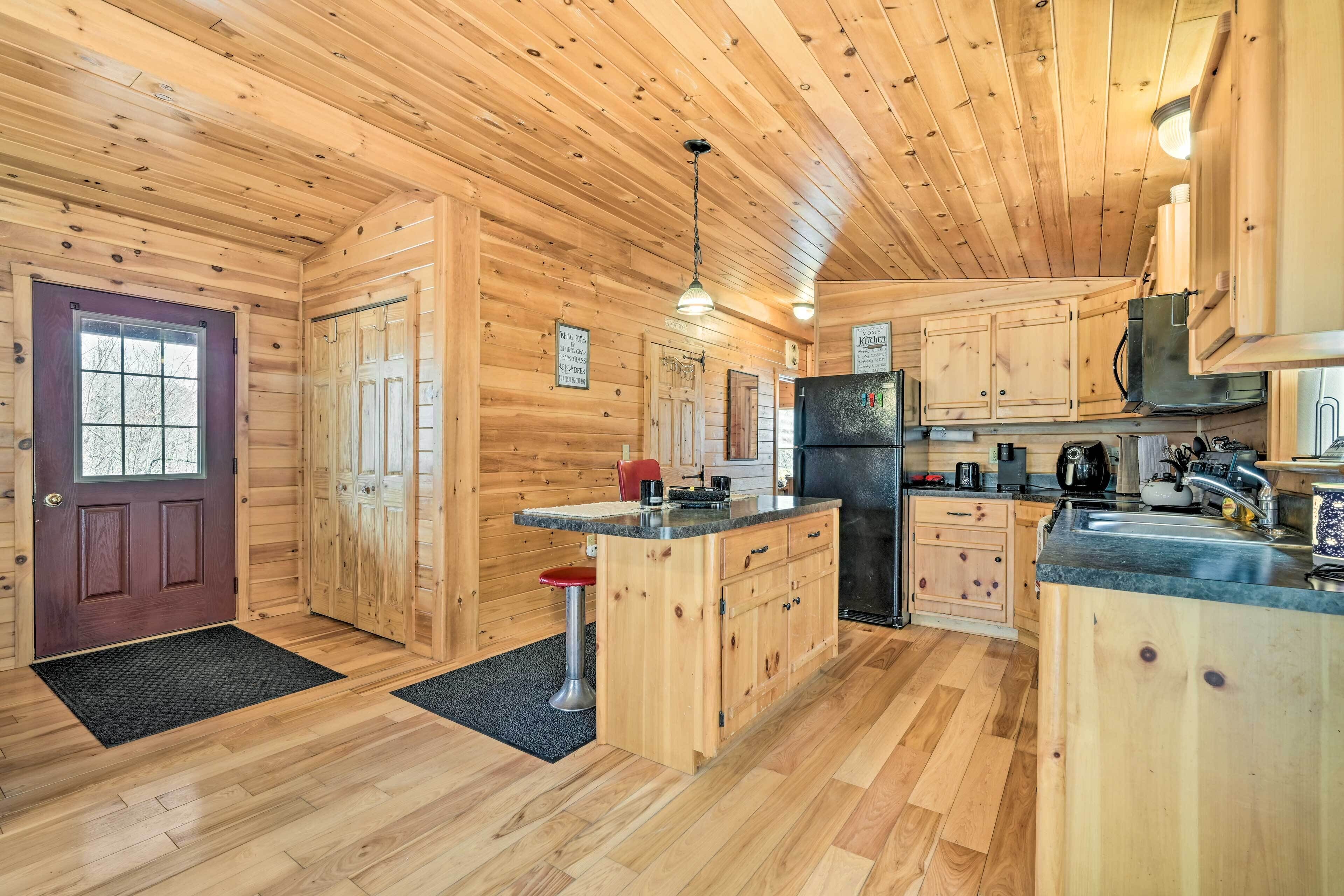 A wooden cabin interior with a kitchen area featuring wooden cabinets, a refrigerator, and a bar stool.
