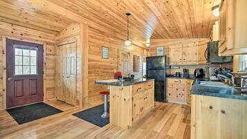 A wooden cabin interior with a kitchen area featuring wooden cabinets, a refrigerator, and a bar stool.