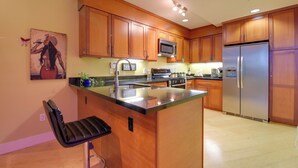 A kitchen with wooden cabinets, a stainless steel refrigerator, a microwave, and a bar stool. - Cozy Emeryville Studio, Near Beaches & Parks! (Emeryville)