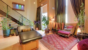A spacious living area with a staircase, multiple potted plants, a comfortable seating area, and a large window with curtains. - Cozy Emeryville Studio, Near Beaches & Parks! (Emeryville)