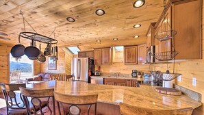 A spacious kitchen with wooden cabinets, a large island with bar stools, hanging pot racks, and a refrigerator.