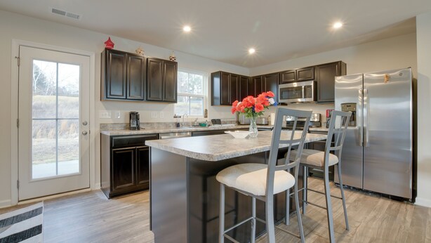 A modern kitchen with dark cabinets, stainless steel appliances, and a central island with bar stools. - 9 Mi to Duke University: Spacious Home w/ Yard! (Durham)