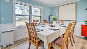 A dining room with a table set for six, wooden chairs, a white tablecloth, and a window with a view of trees. - Cozy Wilmington Vacation Rental: 10 Mi to Beach! (Wilmington)