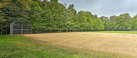 Ein Baseballfeld mit einer Gewächshauskonstruktion, umgeben von dichtem Baumbestand.