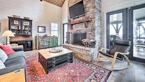 A spacious living room with a stone fireplace, a comfortable seating area, and a large window offering a view of the outdoors.