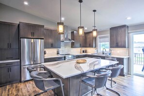 A modern kitchen with dark wood cabinets, stainless steel appliances, a marble island with bar stools, pendant lighting, and a large window providing natural light. - Chic Plymouth Townhome < 1 Mi to Road America (Plymouth)