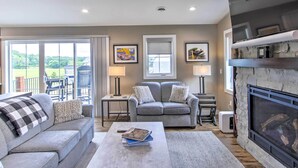 A living room with a fireplace, a sofa, a coffee table, and a view of the outdoors. - Chic Plymouth Townhome < 1 Mi to Road America (Plymouth)