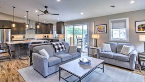 A modern kitchen with a central island, grey sofas, a coffee table, and a ceiling fan. - Chic Plymouth Townhome < 1 Mi to Road America (Plymouth)