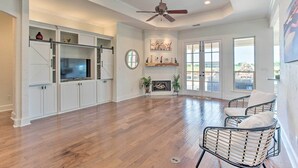 A spacious living room with hardwood flooring, a ceiling fan, a fireplace, and a large window. - Chic Ranch Villa < 5 Mi to Lake Ray Roberts! (Pilot Point)