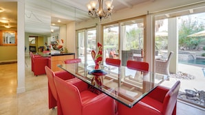 A dining area with a glass table and red chairs, a chandelier, and a view of the outdoor patio. - Near Golfing: Palm Desert Oasis w/ Pool & Spa (Palm Desert)