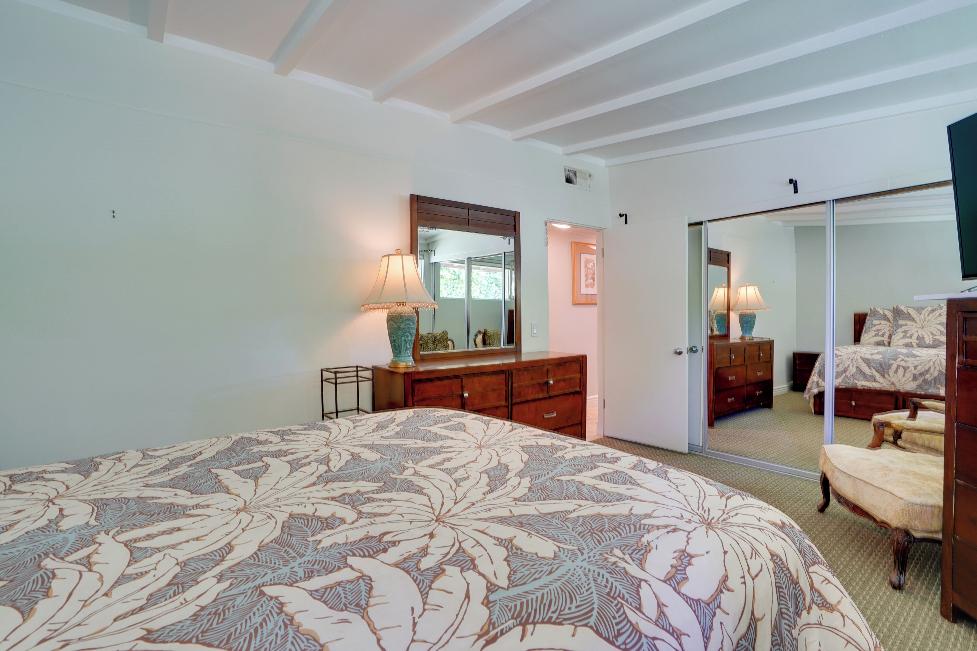 A bedroom with a large bed, a dresser, a mirror, and a sliding door leading to another room.