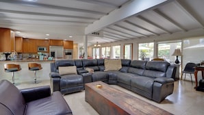 A spacious living room with a large L-shaped sectional sofa, a wooden coffee table, and a kitchen area with wooden cabinets and a refrigerator. - Near Golfing: Palm Desert Oasis w/ Pool & Spa (Palm Desert)