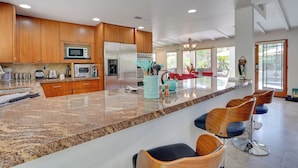 A spacious kitchen with wooden cabinets, a granite countertop, and a central island with bar stools. - Near Golfing: Palm Desert Oasis w/ Pool & Spa (Palm Desert)