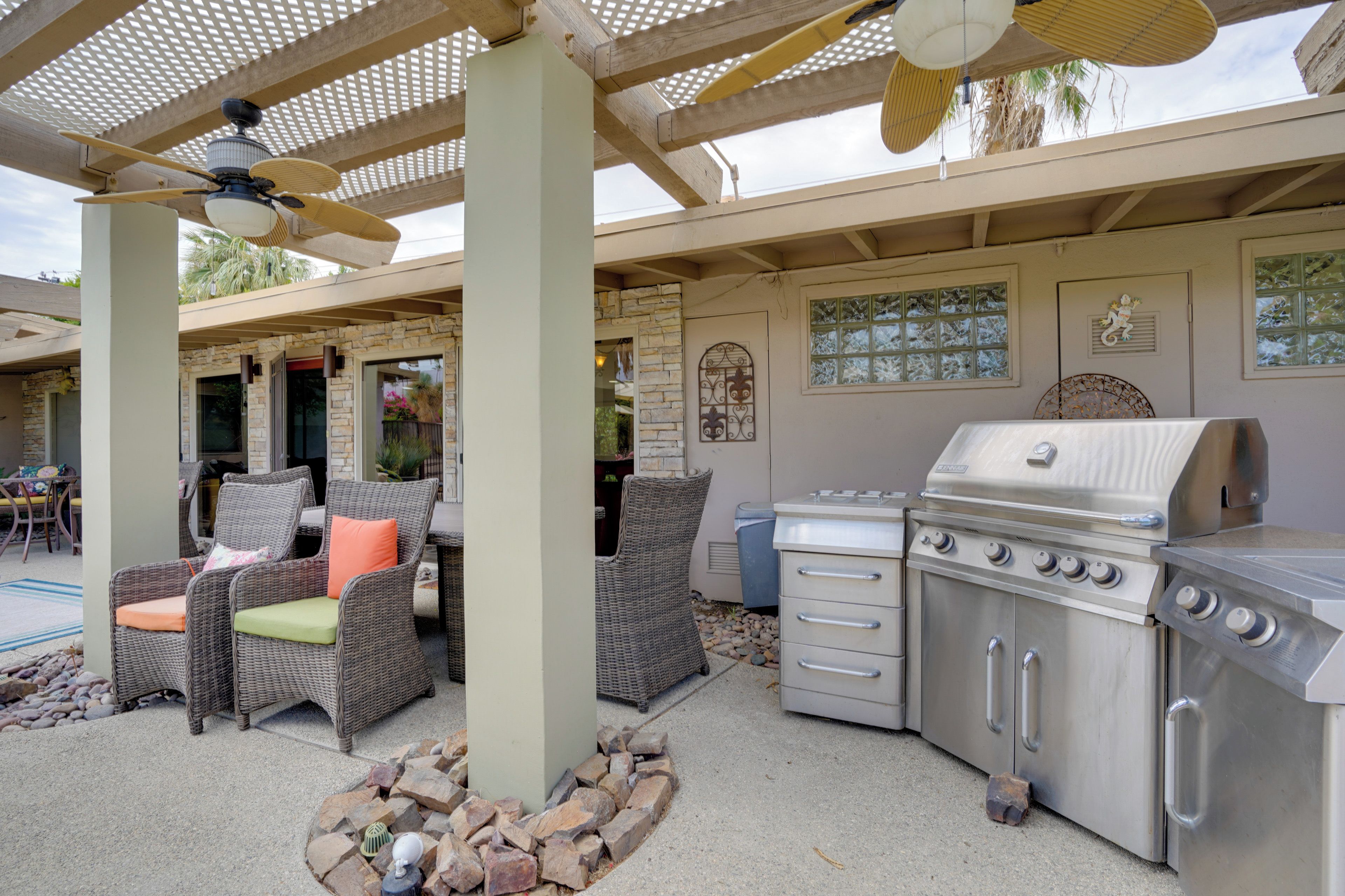 An outdoor patio with wicker furniture, a grill, and a pergola with a ceiling fan.