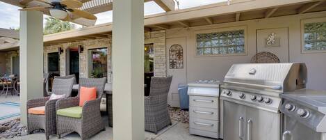 An outdoor patio with wicker furniture, a grill, and a pergola with a ceiling fan.