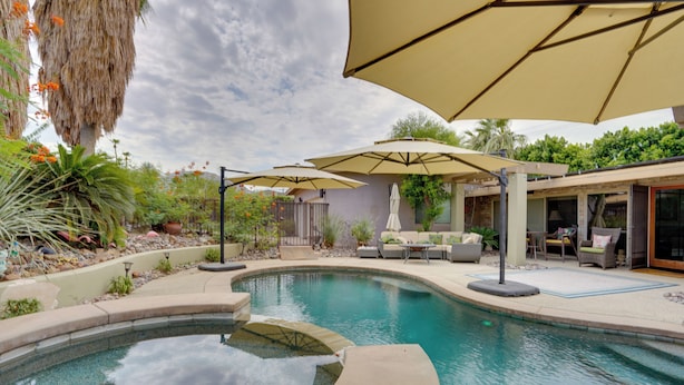 A swimming pool with a curved edge, surrounded by outdoor furniture and umbrellas. - Near Golfing: Palm Desert Oasis w/ Pool & Spa (Palm Desert)