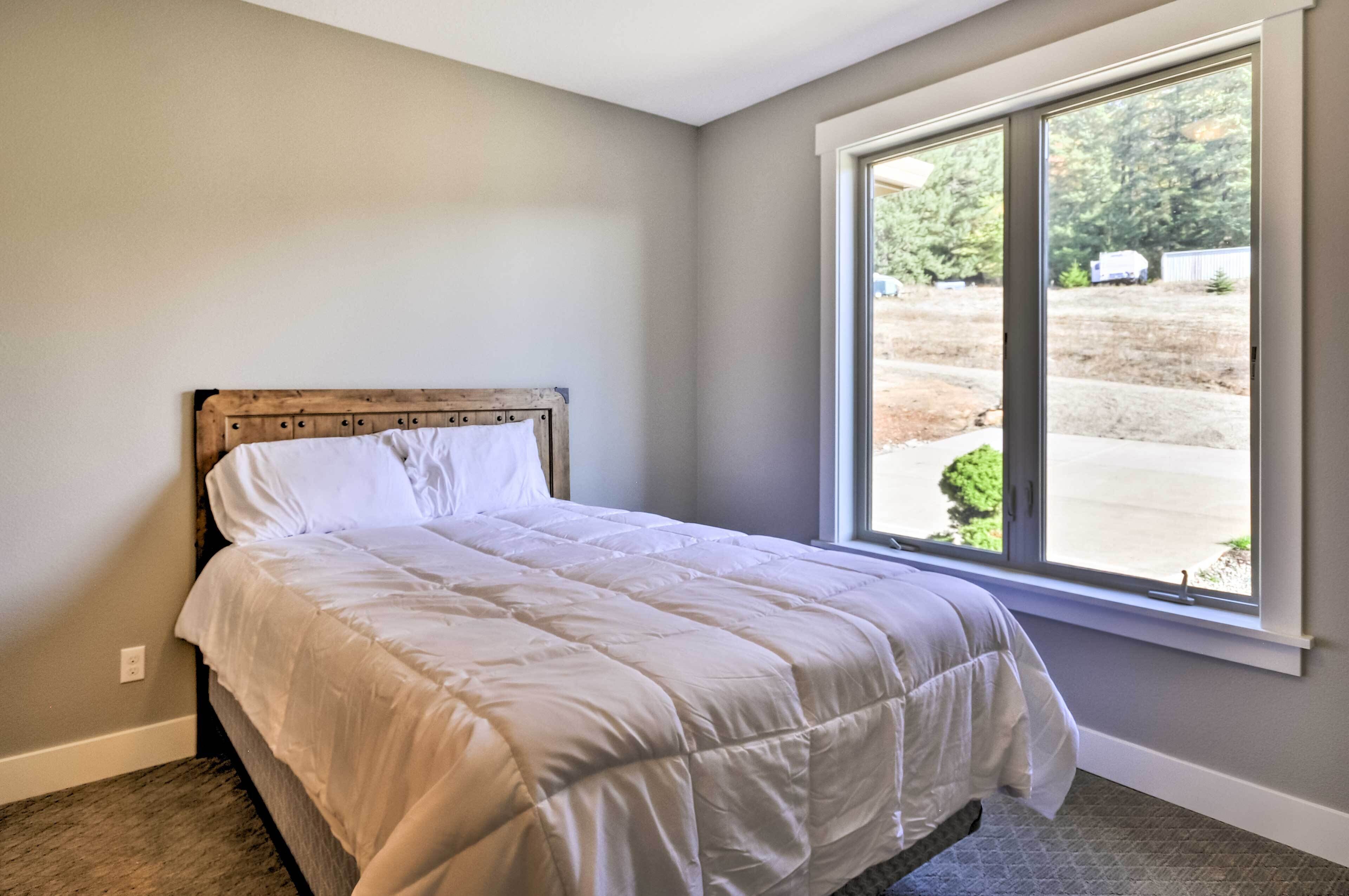 A bedroom with a large window, a wooden headboard, and a white bedspread.