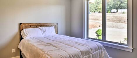 A bedroom with a large window, a wooden headboard, and a white bedspread.