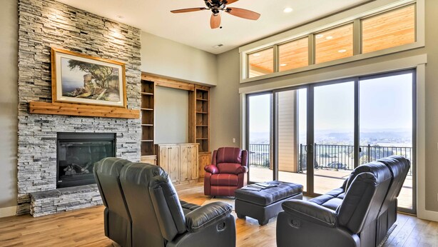 A spacious living room with a stone fireplace, leather sofas, a red chair, and a balcony with a view.