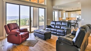 A spacious living room with leather recliners, a large sliding glass door leading to a balcony, and a modern kitchen in the background.