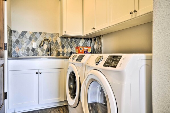 A laundry area with two front-loading washing machines, a tiled backsplash, and white cabinetry.