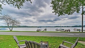 Une vue sur le lac, avec des chaises et un foyer, des bateaux amarrés au loin et un ciel nuageux.