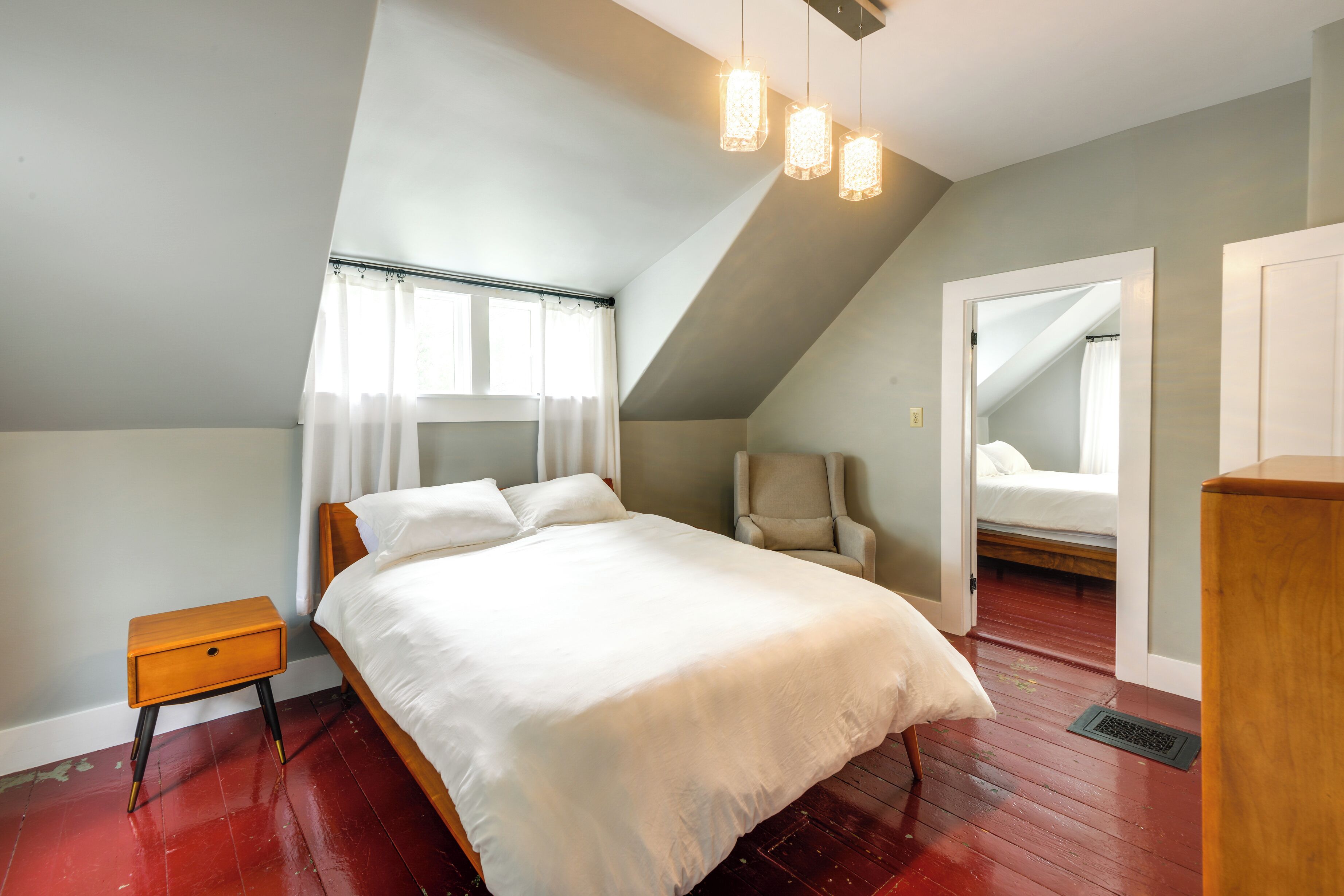 A bedroom with a bed, a nightstand, a chair, and a door leading to another room.