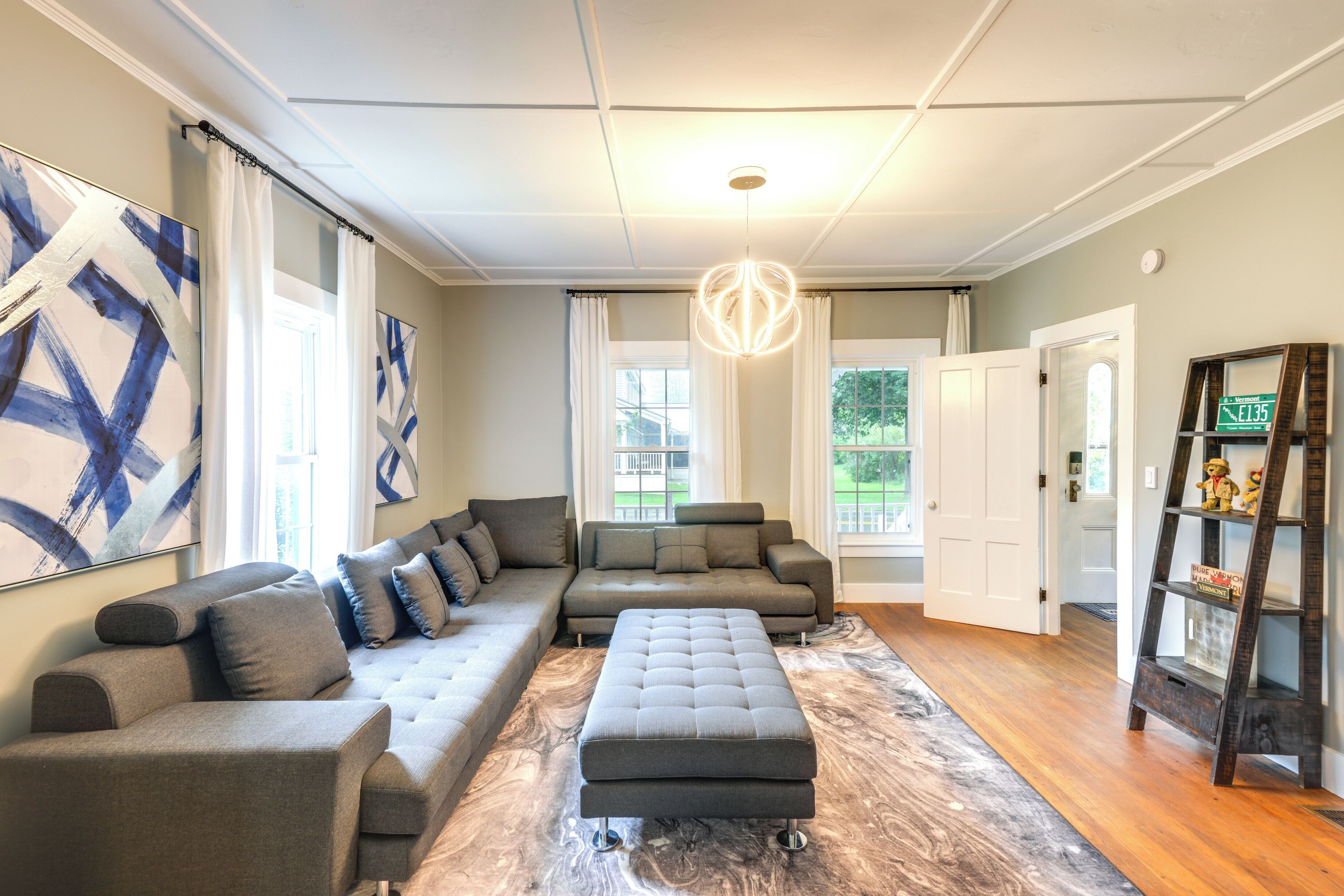 A modern living room with a sectional sofa, ottoman, and a decorative ladder shelf.