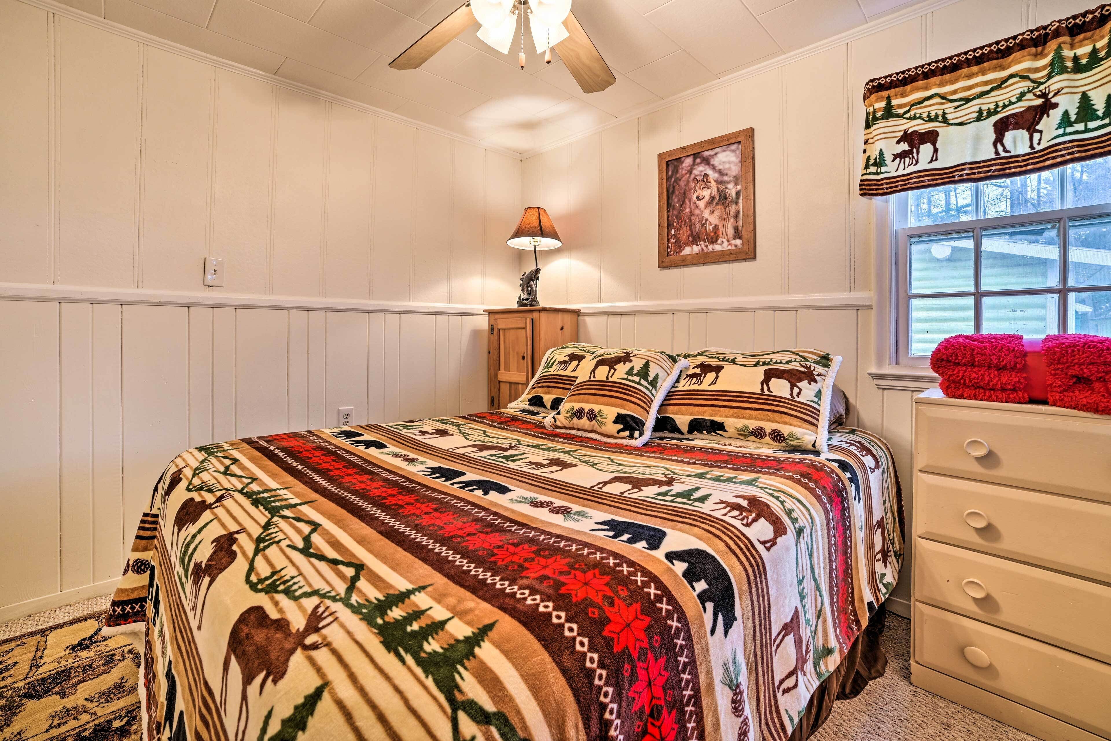 A bedroom with a large bed, a nightstand, a lamp, a window with a view, and a wall with a painting.