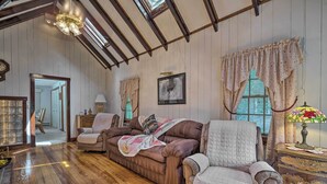 Una habitación acogedora con suelo de madera, un sofá marrón, un sillón blanco y un mueble de madera con una lámpara.