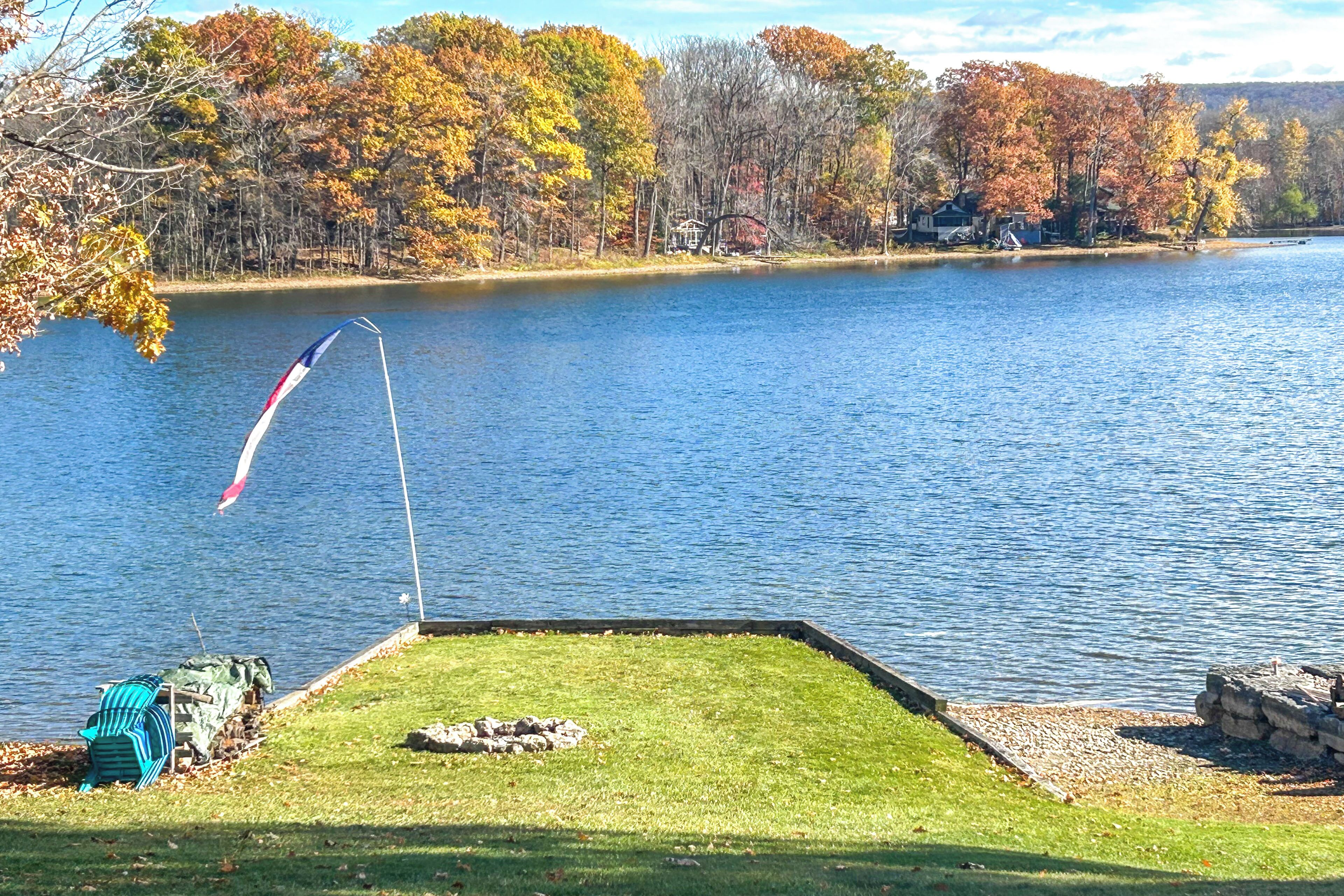 A lakeside view with a grassy area, a flag, and autumn-colored trees.