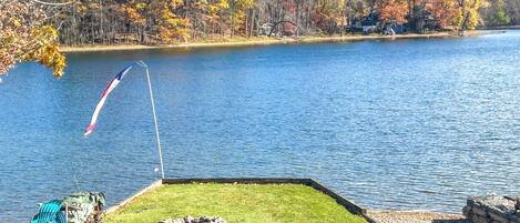 A lakeside view with a grassy area, a flag, and autumn-colored trees.