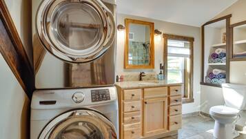 A laundry area with stacked washing machines, a wooden cabinet, a sink, and a toilet.