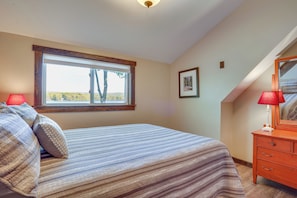 A bedroom with a large window, a bed with striped bedding, a dresser with a mirror, and a framed picture on the wall. - Family Friendly! Lakefront Tully Getaway w/ Porch (Tully)
