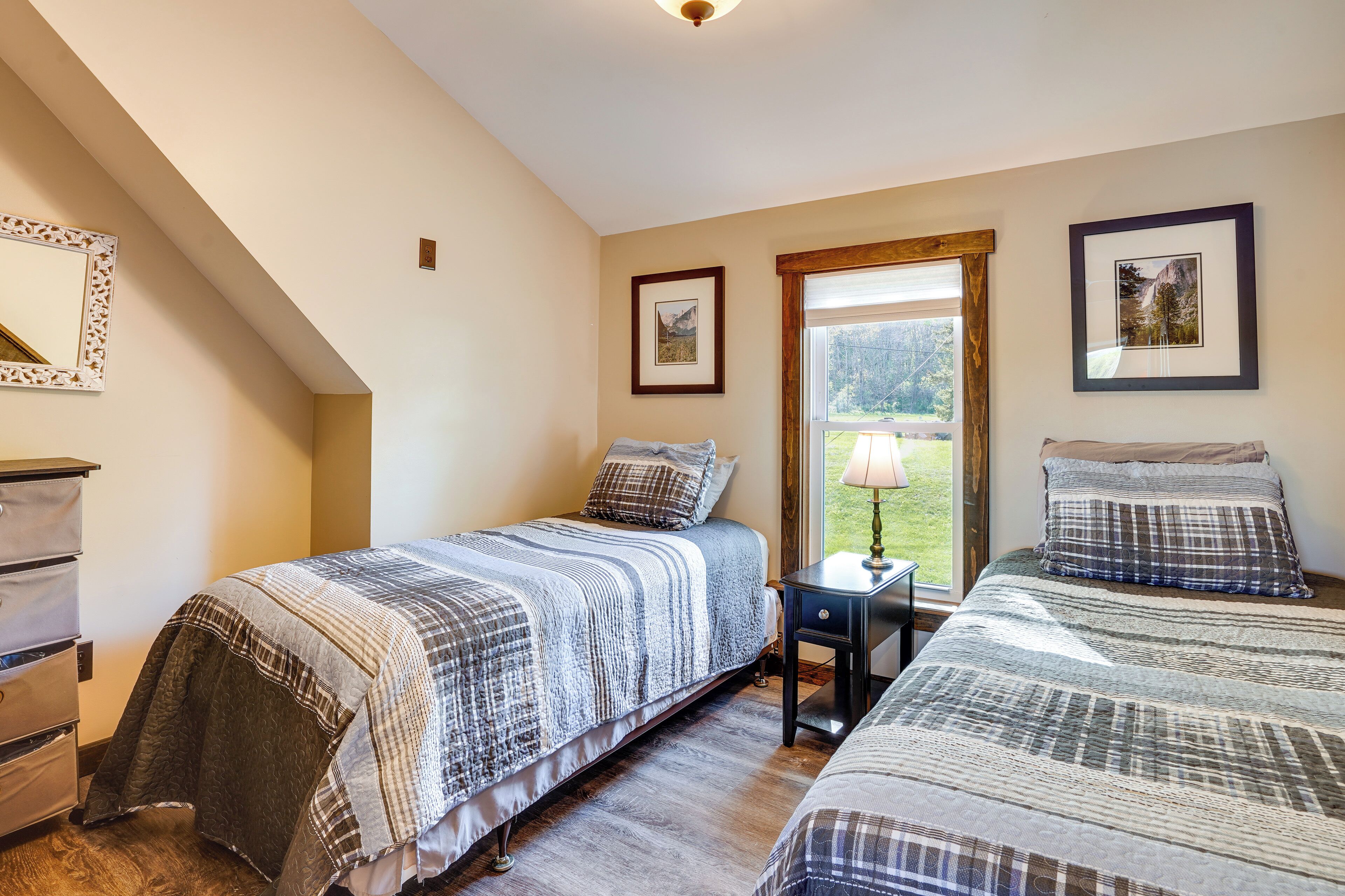 A bedroom with two beds, a dresser, and a window with a view of the outdoors.