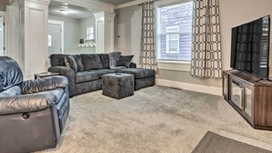 A living room with a sectional sofa, ottoman, and a dark wooden entertainment center. - Charming Greencastle Home < 1 Mi to Depauw! (Greencastle)