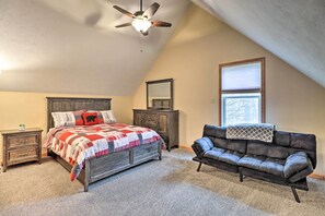 A bedroom with a bed, a dresser, a leather sofa, a ceiling fan, and a window.