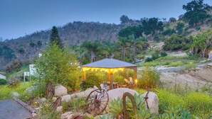 A gazebo with string lights, surrounded by rocks, succulents, and a hillside backdrop.