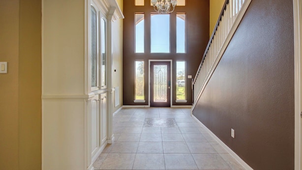 A hallway with a grand staircase, large windows, and a door leading outside.