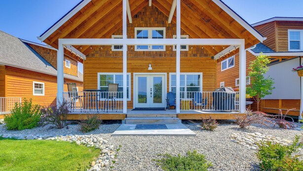 Ein zweistöckiges Holzhaus mit Veranda, einer kleinen Terrasse und einer Schotterauffahrt.