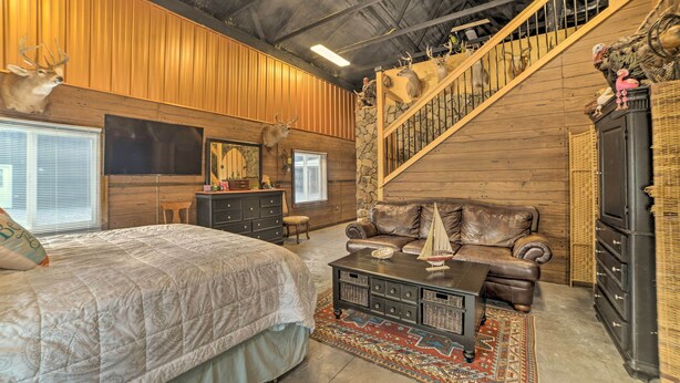 A room with a bed, a leather sofa, a staircase, and mounted animal heads on the wall. - Family Leatherwood Resort Cabin w/ Fire Pit! (Dover)