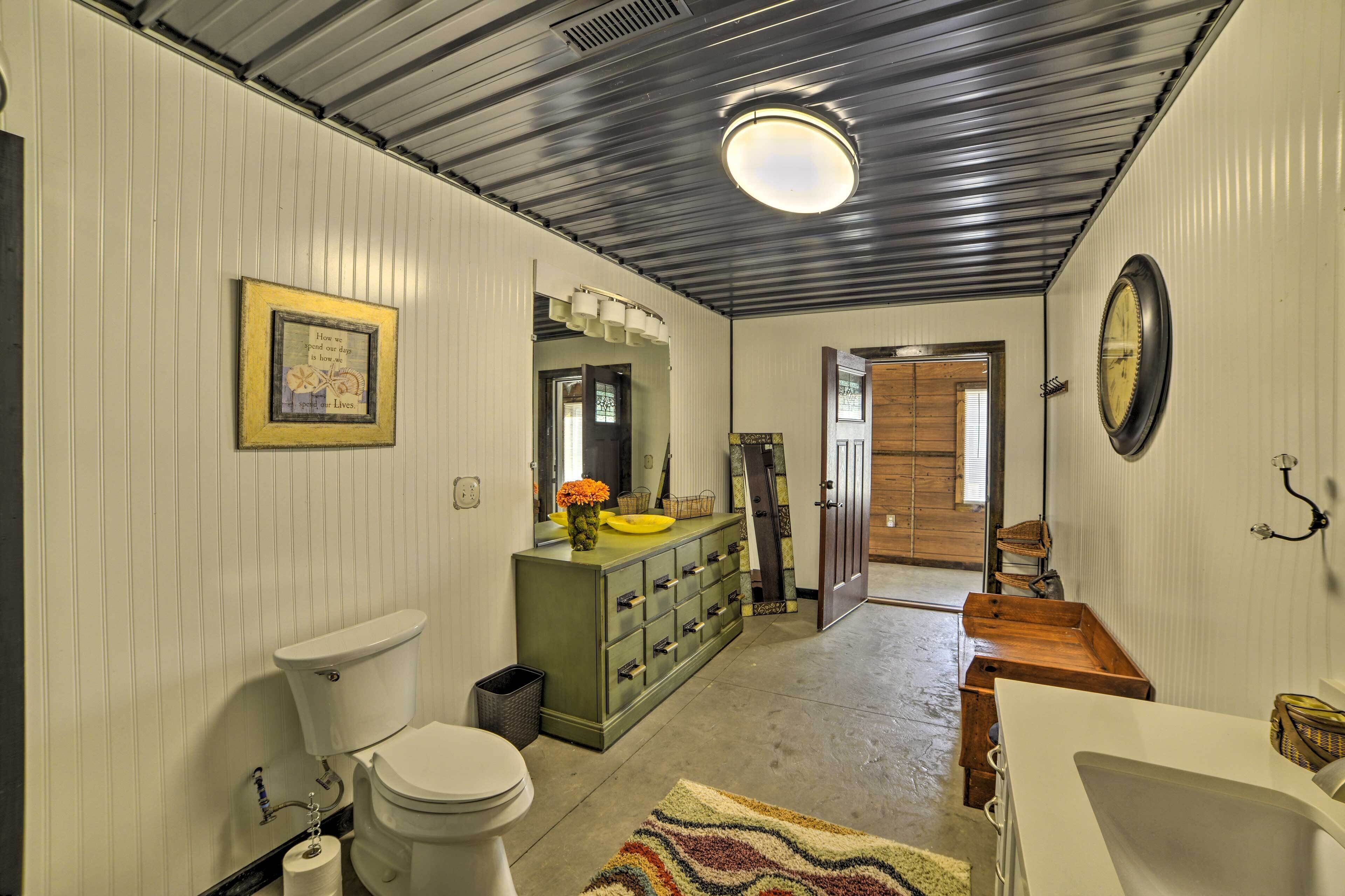 A bathroom with a toilet, sink, and vanity. There is a mirror above the vanity and a clock on the wall.