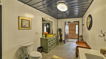 A bathroom with a toilet, sink, and vanity. There is a mirror above the vanity and a clock on the wall.