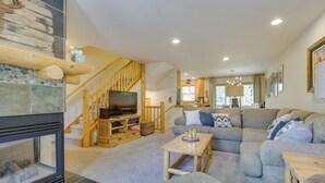 A cozy living room with a fireplace, a wooden staircase, a large gray sectional sofa, and a television. - Downtown Winter Park Townhouse 3 Mi to Ski Resort! (Winter Park)