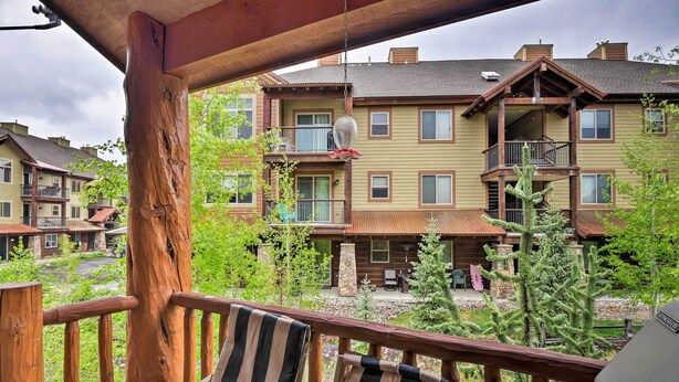 A wooden deck with two striped chairs and a small table, overlooking a residential area with multi-story buildings and a view of a mountain. - Downtown Winter Park Townhouse 3 Mi to Ski Resort! (Winter Park)